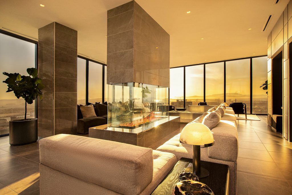Interior of modern living room with couch, fireplace, and city view out the wall of windows.