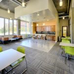 Common room with tables and chairs and a kitchen on the back wall.