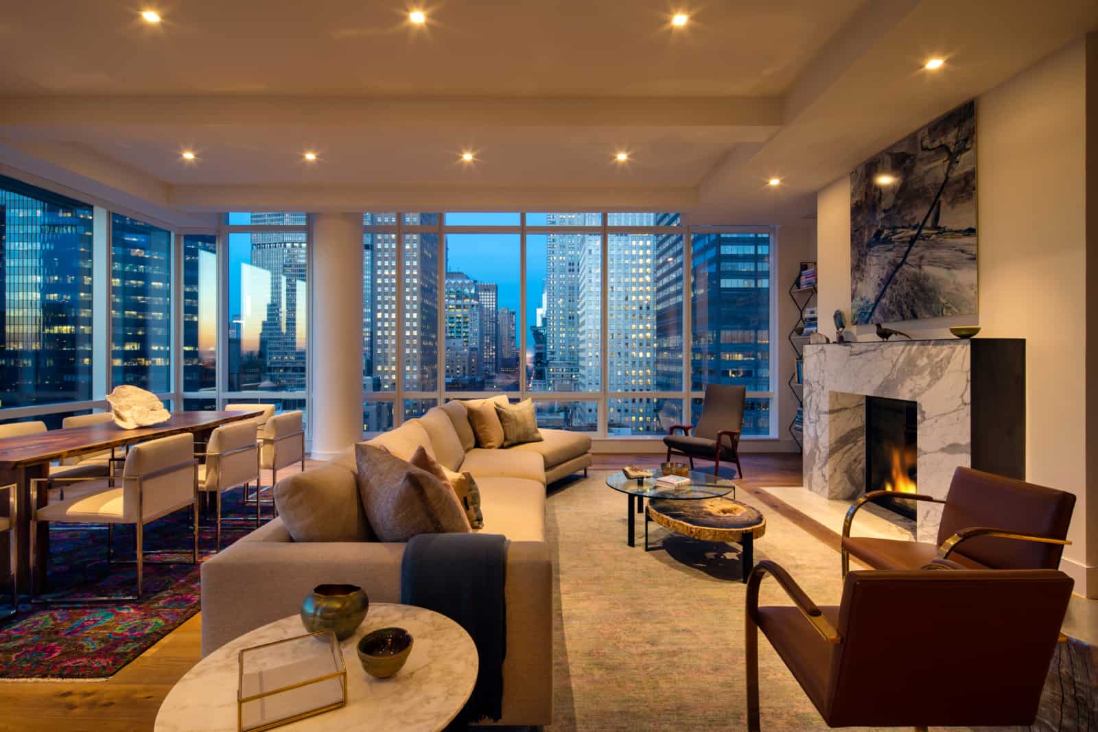 Large open plan apartment with living room area with fireplace, dining table, and windows on two sides with city views.