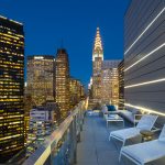 Exterior of large balcony with seating amidst downtown New York skyscrapers.