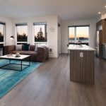 Interior of modern apartment with open kitchen, seating area with windows on two walls.