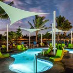 Exterior of aomebaic-shaped pool surrounded by modern deck chairs and palm trees.