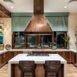 Interior of large kitchen with stainless steel appliances, central island with cooktop and seating.