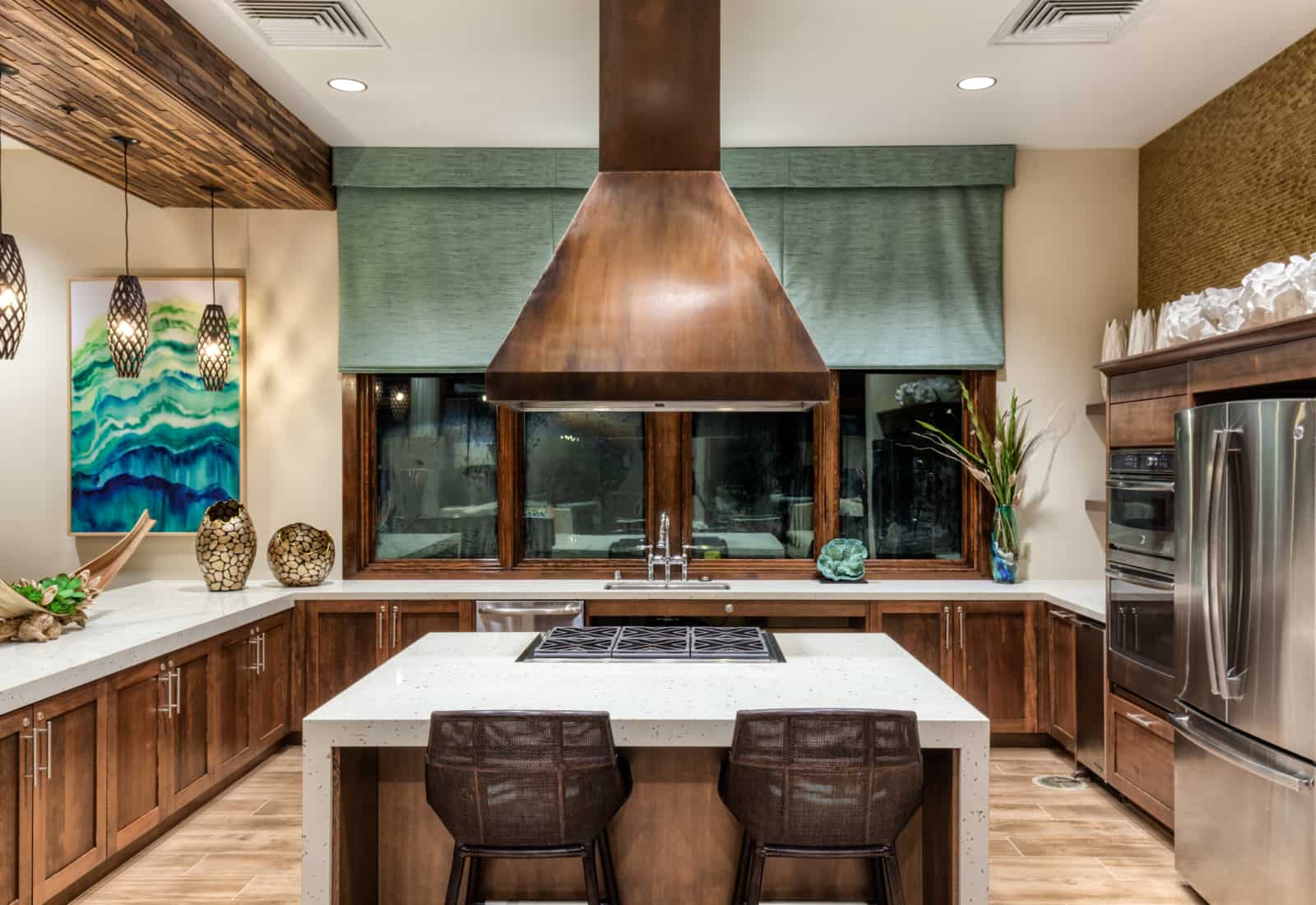 Interior of large kitchen with stainless steel appliances, central island with cooktop and seating.