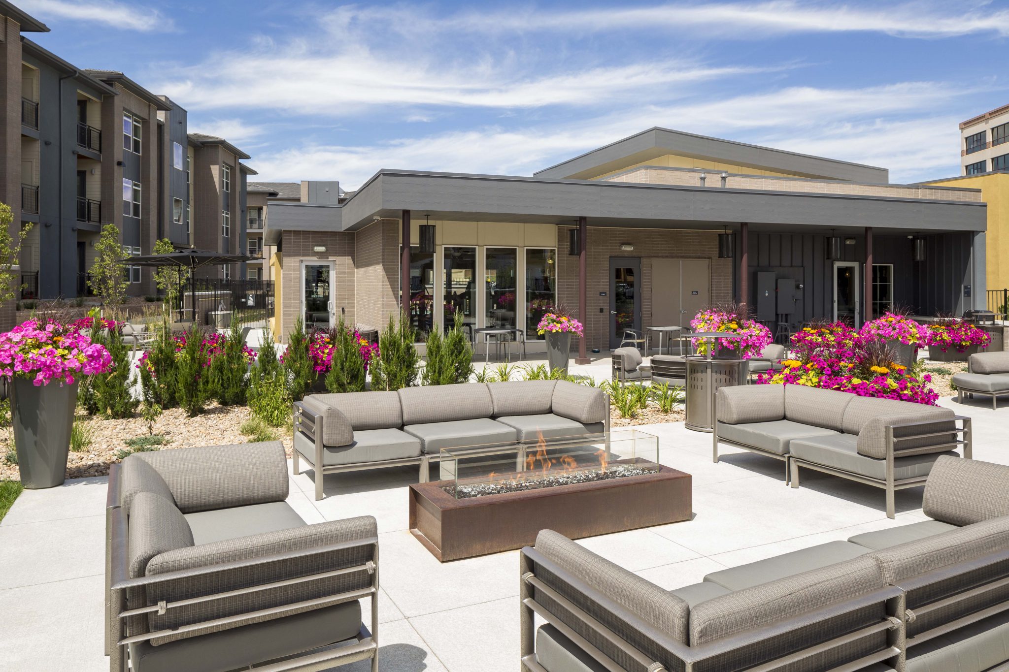 Exterior of glass-walled fire pit and couches with apartment buildings in the background