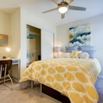 Interior of apartment bedroom with bed, closet, desk and ceiling fan