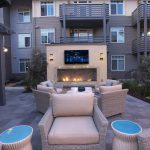 Exterior common area with seating, fireplace and large-screen television surrounded by apartment buildings