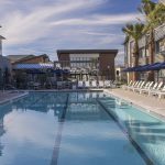 Exterior of pool with lounge chairs, umbrellas, and cabanas surrounded by apartment complex