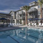 Exterior of pool with lounge chairs and umbrellas with 3-story apartment building with balconies in the background