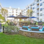 Exterior of courtyard between buildings with grass, seating around a fire pit, barbeques, and table seating.