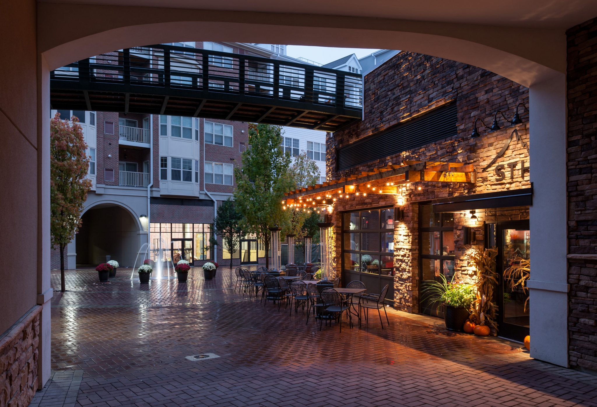 Exterior of courtyard with restaurant, fountain, and overhead walkway with apartment building in background