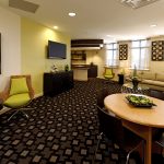 Interior of the common area with couches, chairs, tables, TV, and kitchen in the background.