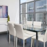 Interior of dining area with glass and steel table and white leather chairs.