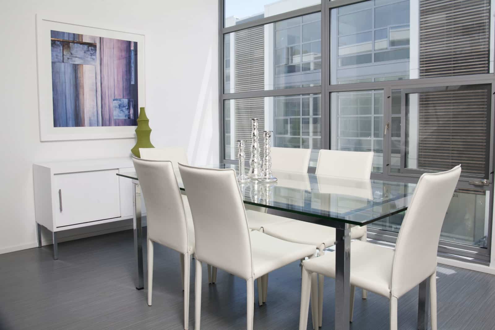 Interior of dining area with glass and steel table and white leather chairs.