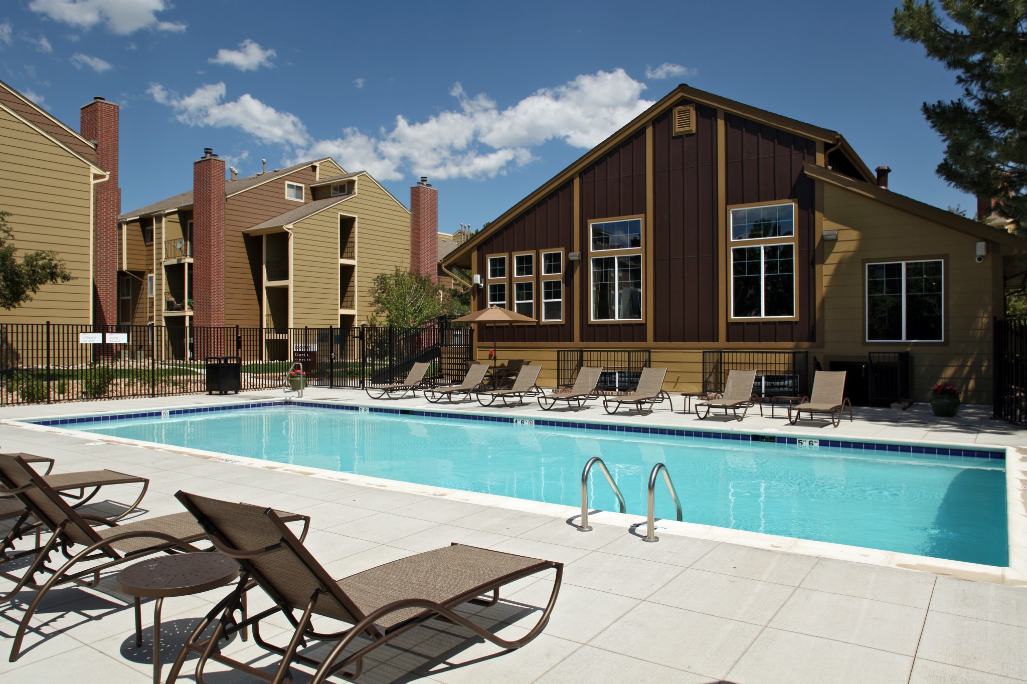 Outdoor pool area with lounge chairs and apartment building in the background.