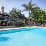 Outdoor pool surrounded by lounge chairs, trellis, trees, and apartment building in the background.