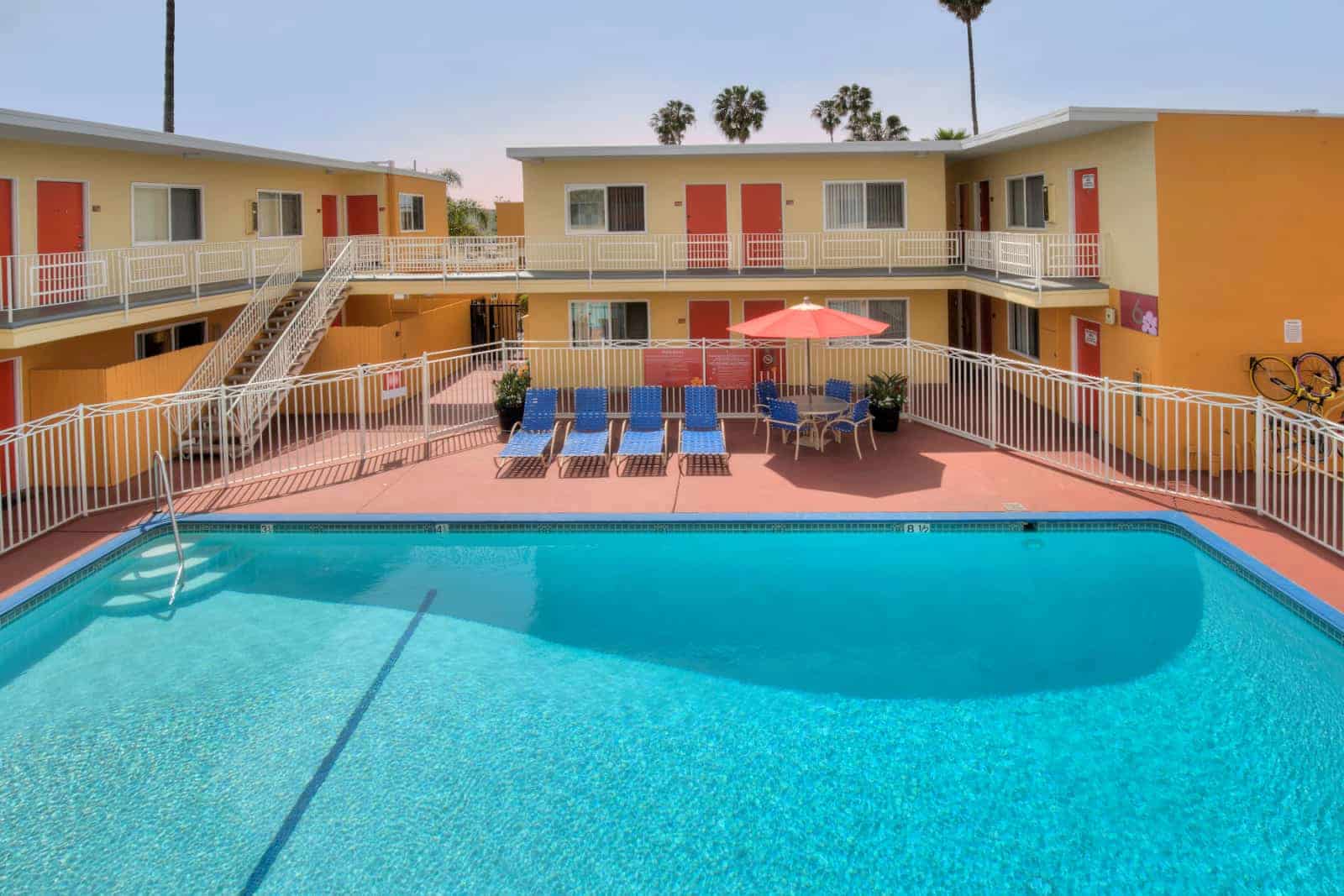View of the pool surrounded by a white fence and the apartment building in the background.