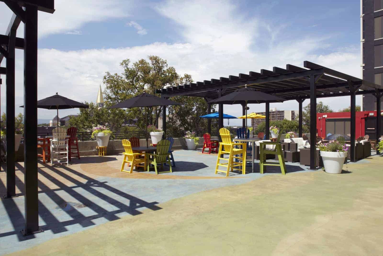 Roofdeck with adirondack chairs and barstools, couches, tables, umbrellas, and trellis.