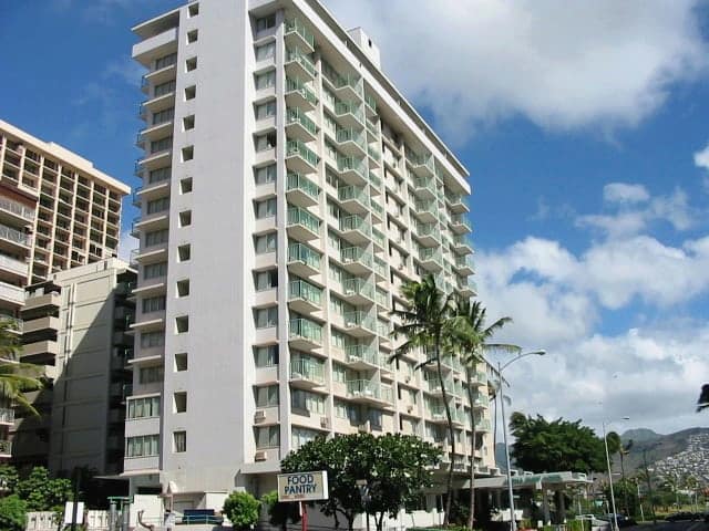 Exterior of a tall apartment building against a cloudy blue sky.