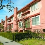 Exterior of entrances to units with a hedge, sidewalk and trees in front of the building.