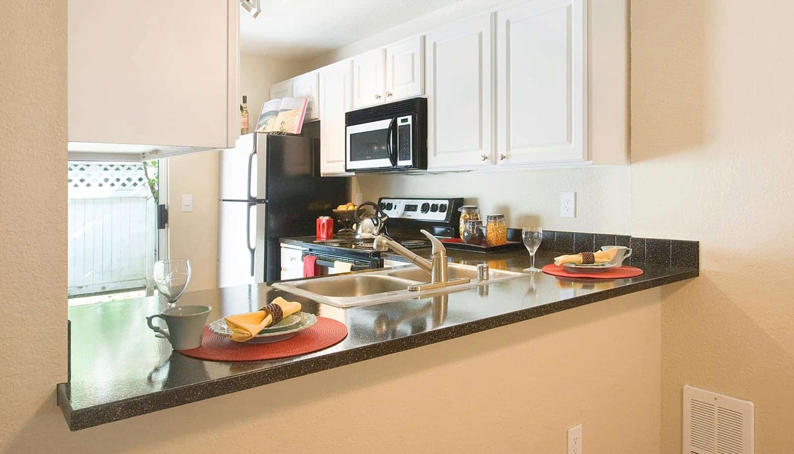 Ktichen with stainless steel appliances, black countertops, and white cabinets.