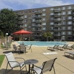 View of the pool area with lounge chairs, tables and umbrellas with the building in the background.