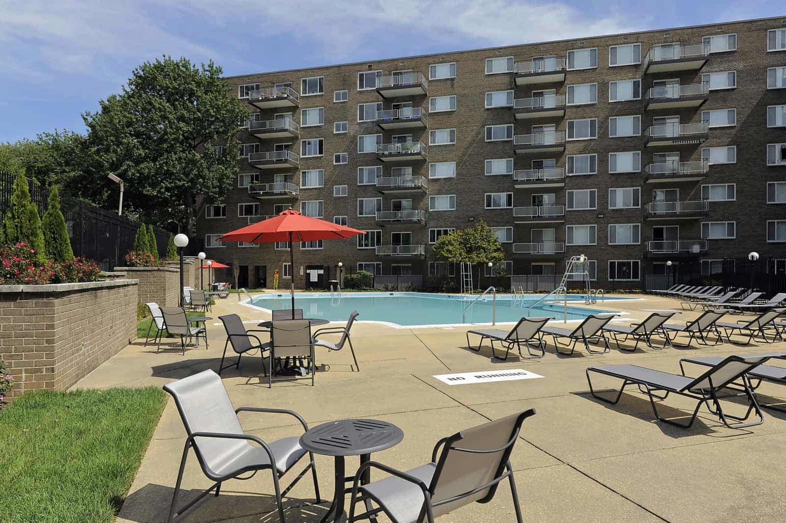View of the pool area with lounge chairs, tables and umbrellas with the building in the background.