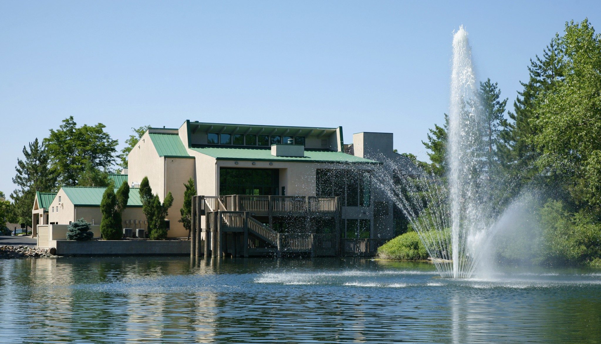 View of lake and fountain with building and trees in the background.