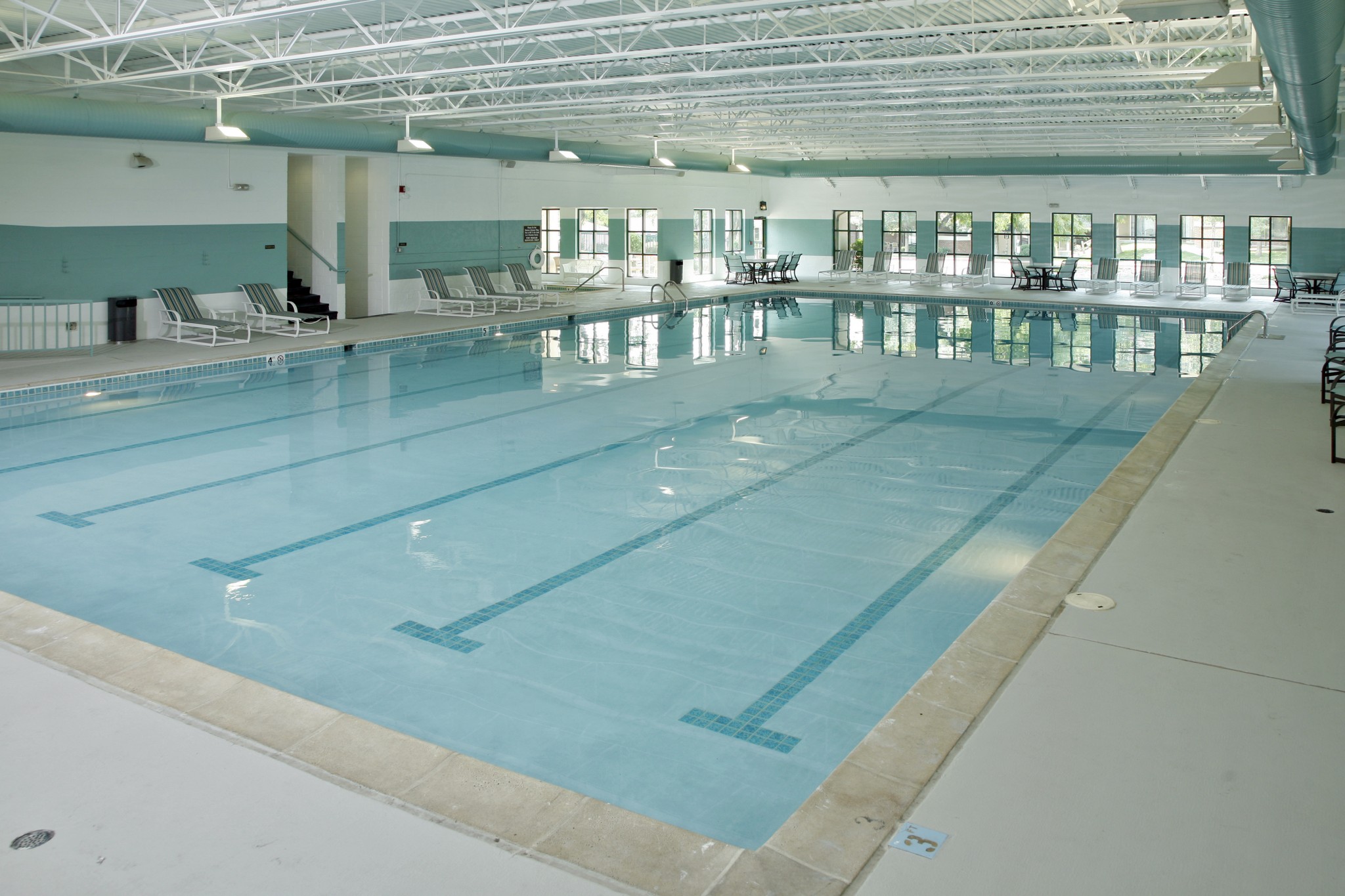 Indoor lap pool surrounded by lounge chairs and tables.