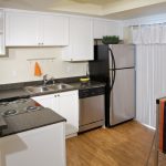 Apartment kitchen with stainless steel appliances, black countertop and white cabinets..