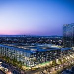 Aerial exterior of 6-story apartment complex filling city block and 14-story apartment tower