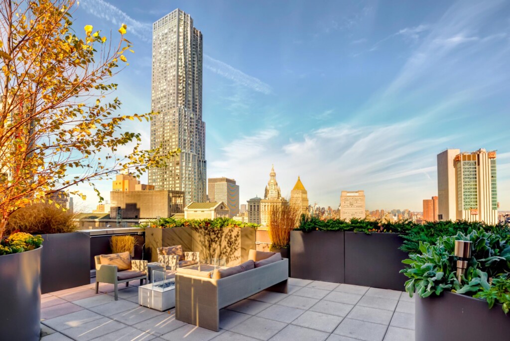 Exterior of rooftop appointed with metal planters and a seating area with fire pit, surround by other New York buildings.