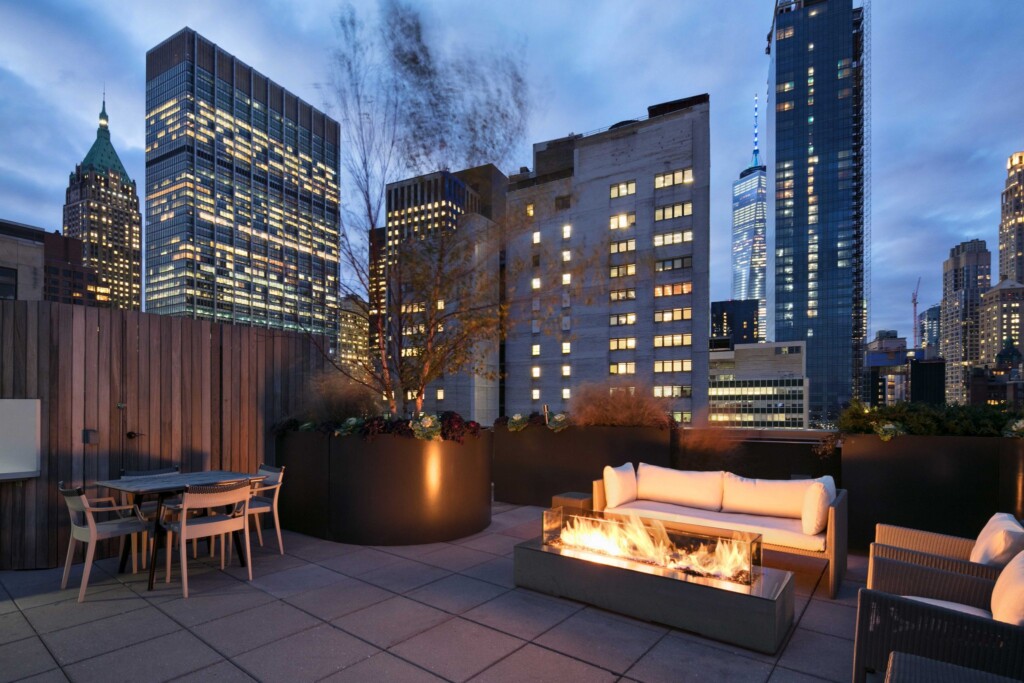 Exterior of rooftop with fire pit, couch and dining table with other downtown New York buildings in background