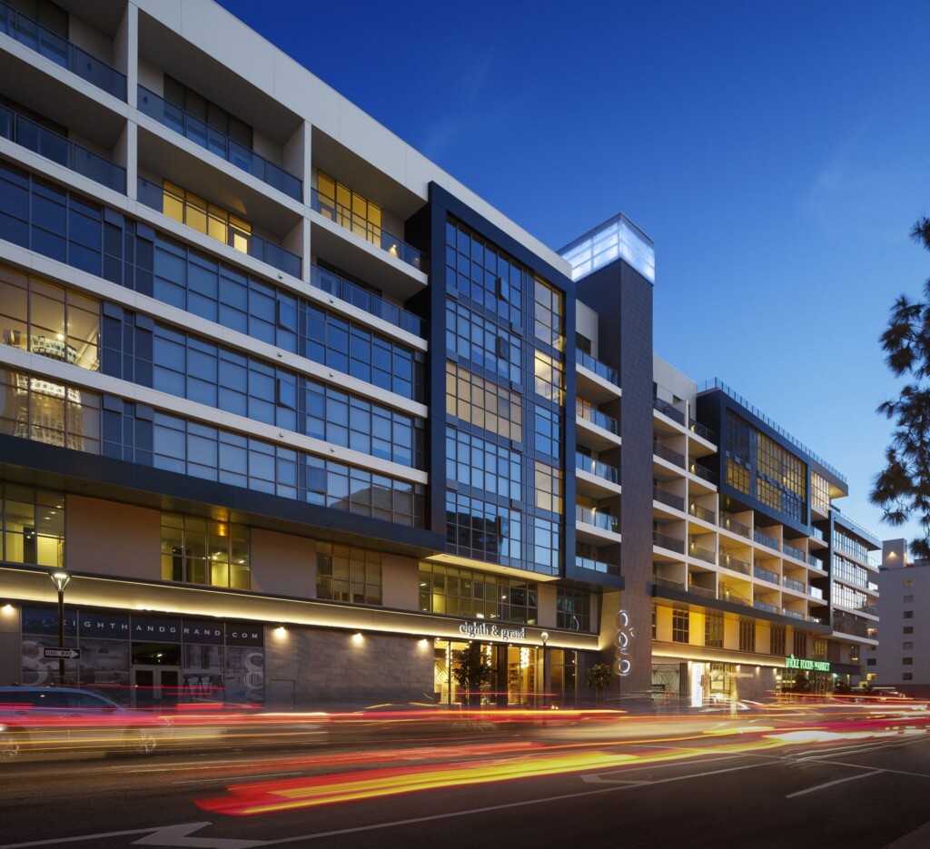 Street-level exterior of six-story modern apartment building with cars' tail lights blurred in foreground.