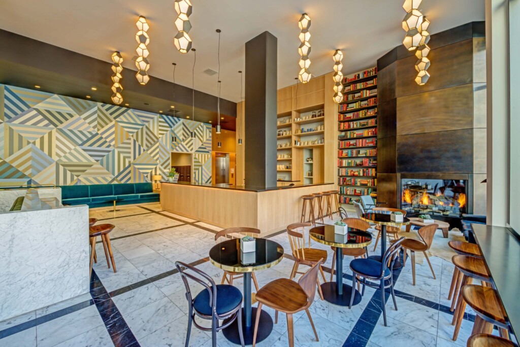 Interior of common area with high ceiling, small tables and chairs, fireplace, and book shelves.