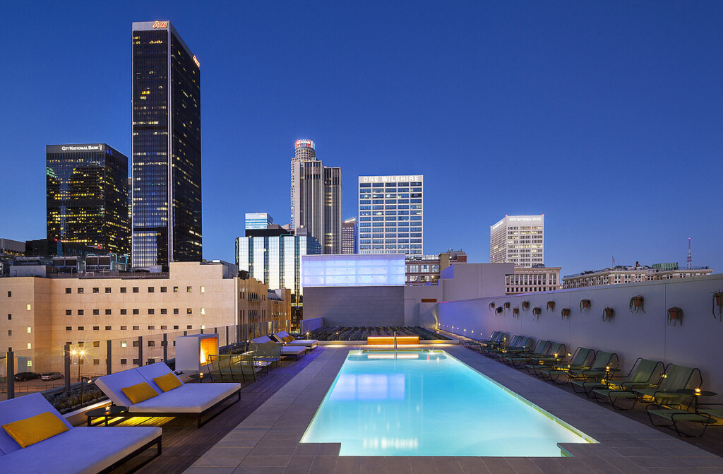 Rooftop pool exterior with chaise lounges and downtown Los Angeles buildings in background.