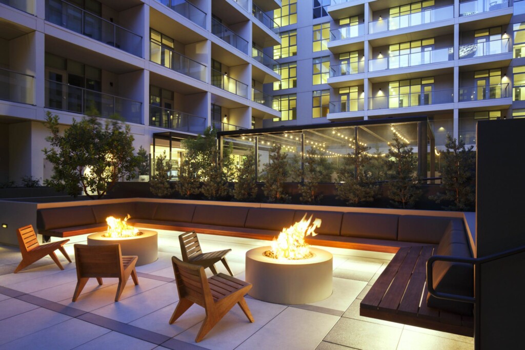 Outdoor seating area with two fire pits and apartment building in background.