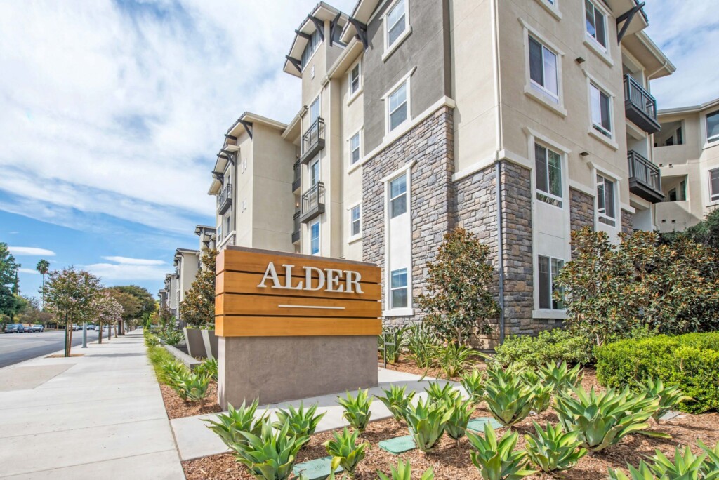 Street-level exterior of Alder sign with apartment building to right and tree-lined street to the left