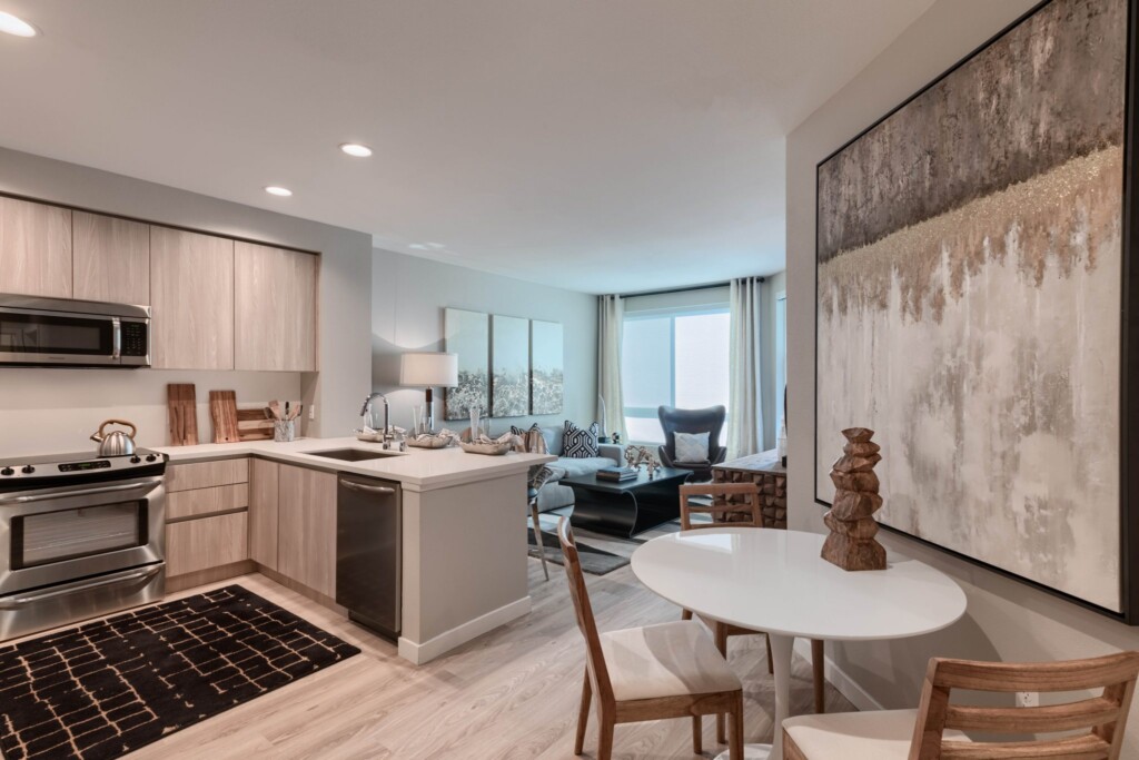 Apartment interior of open-plan kitchen with dining table and living room in background