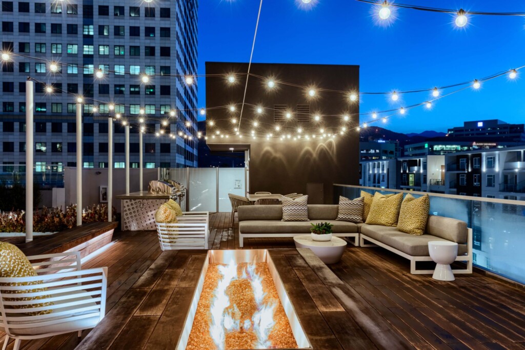 Exterior of rooftop seating area with fire pit and cafe lights overhead