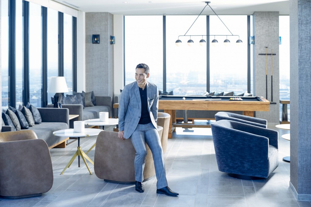 Interior with man in suit leaning on the back of a chair in a modern game room with pool table and city views ch