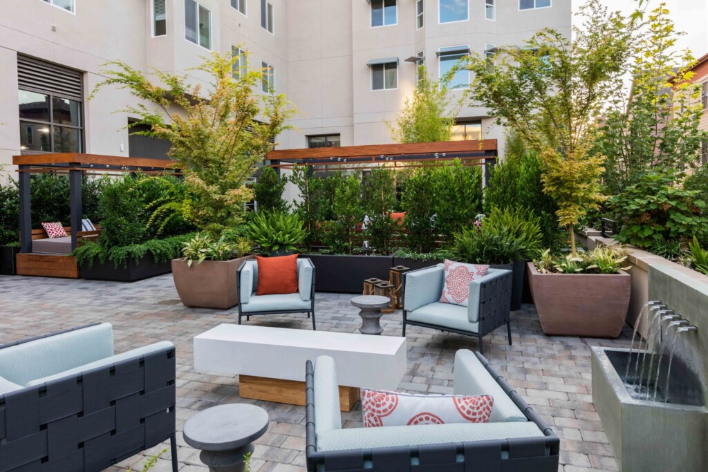 Common outdoor area with chairs, fountain and lush vegetation.