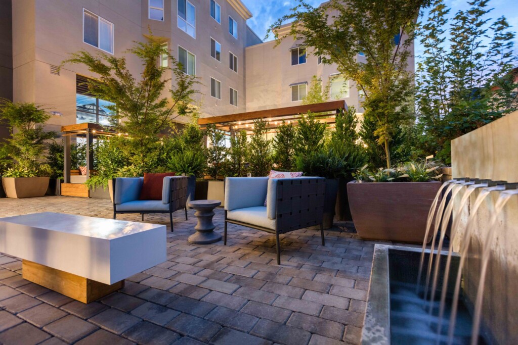 Common outdoor area with chairs, fountain and lush vegetation.