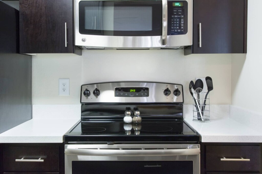 Stainless steel microwave and oven, electric cooktop in kitchen with white counter tops and dark cabinets.