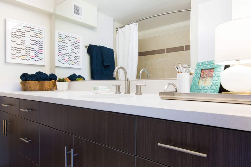 Apartment bathroom vanity with shower reflected in large vanity mirror.