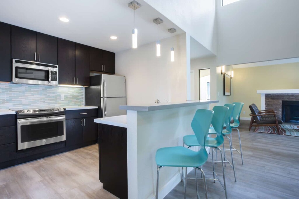 Interior with open plan kitchen, bar height seating and chairs beside fireplace in background.