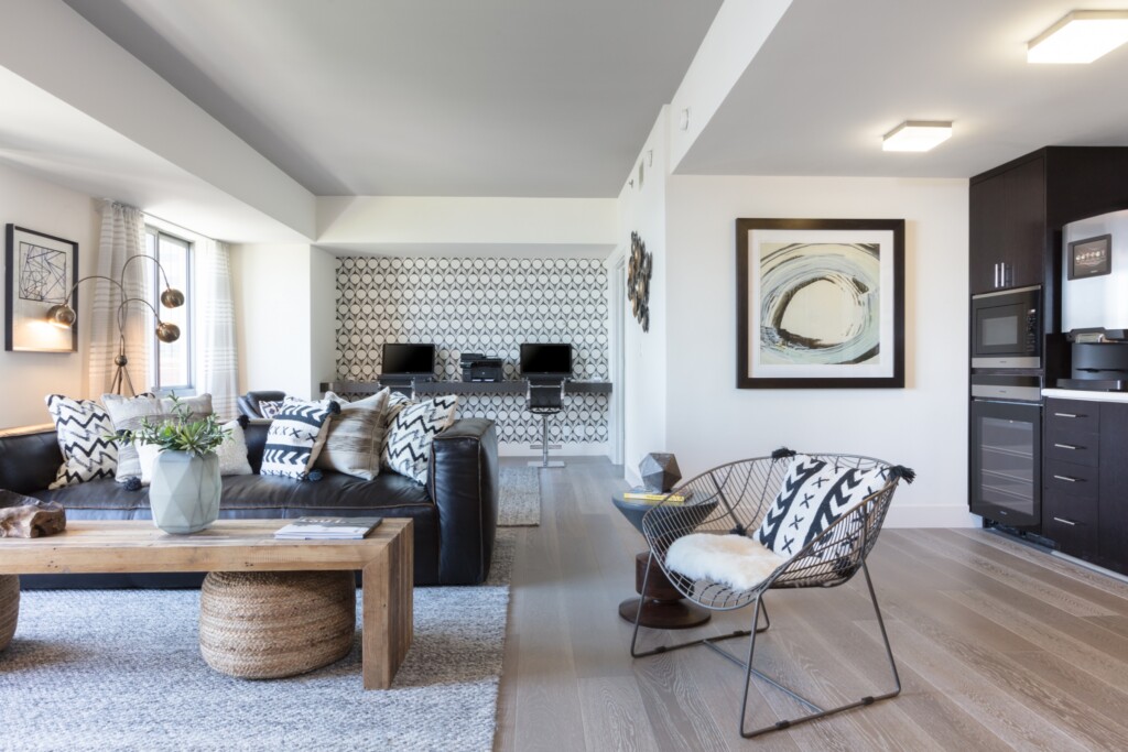 Common area with couch, coffee table, chair, kitchen area and two computer stations in the background.