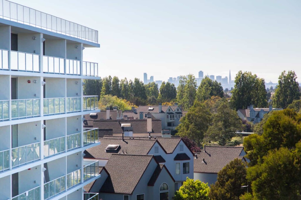 White apartment building with glass balcony railings and cityscape in background.