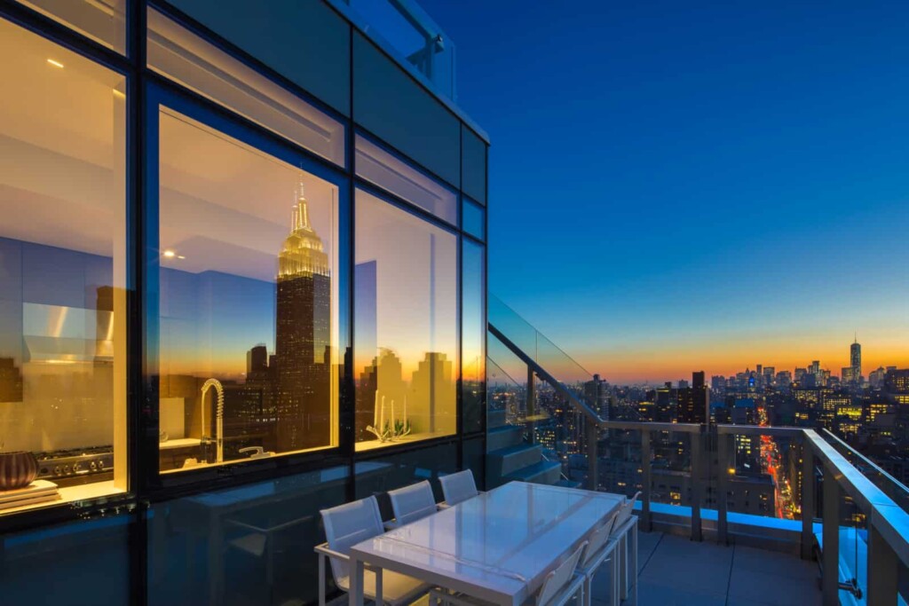 Exterior of balcony with dining table looking into apartment kitchen with city skyline in background.