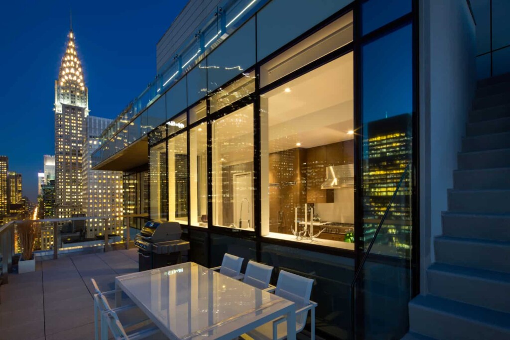 Exterior of balcony with dining table looking into apartment kitchen with city in background.